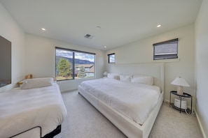 A hotel room with two beds, a large window with a mountain view, a ceiling vent, and a bedside table with a lamp. - Big Sky Luxury: Modern 4BR, Heated Patio, Fire Pit, Hot Tub, Views, Walk to Town (Big Sky)