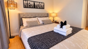 A hotel room with a bed, a wall-mounted lamp, a bedside table with a lamp, and a 'NEW YORK' sign. -     Cozy Comfort Suite (Vancouver)