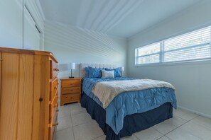 A bedroom with a bed, a wooden dresser, a nightstand, and a window with blinds. - Coastal 2BR on the Canal near Anna Maria (Bradenton)