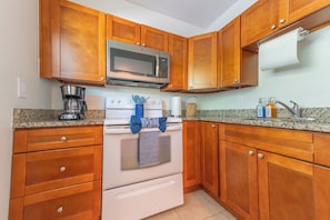 A kitchen with wooden cabinets, a microwave, a stove, a coffee maker, and a sink. - Coastal 2BR on the Canal near Anna Maria (Bradenton)