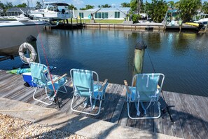 A dock with three striped lounge chairs and a cooler, a fishing rod, and a life preserver. - Coastal 2BR on the Canal near Anna Maria (Bradenton)