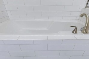 Une salle de bain avec une baignoire blanche, un seul robinet et des murs recouverts de carreaux blancs.