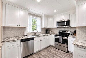 A modern kitchen with white cabinets, stainless steel appliances, a marble countertop, and a window with a view of greenery. - Fenced yard - Quiet Street - Walkable (Dayton)