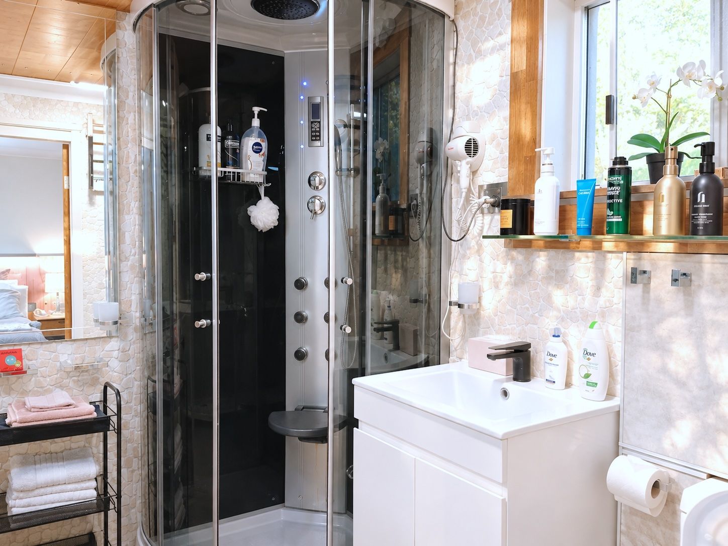 A modern bathroom with a glass-enclosed shower, a white sink, and a shelf with toiletries.