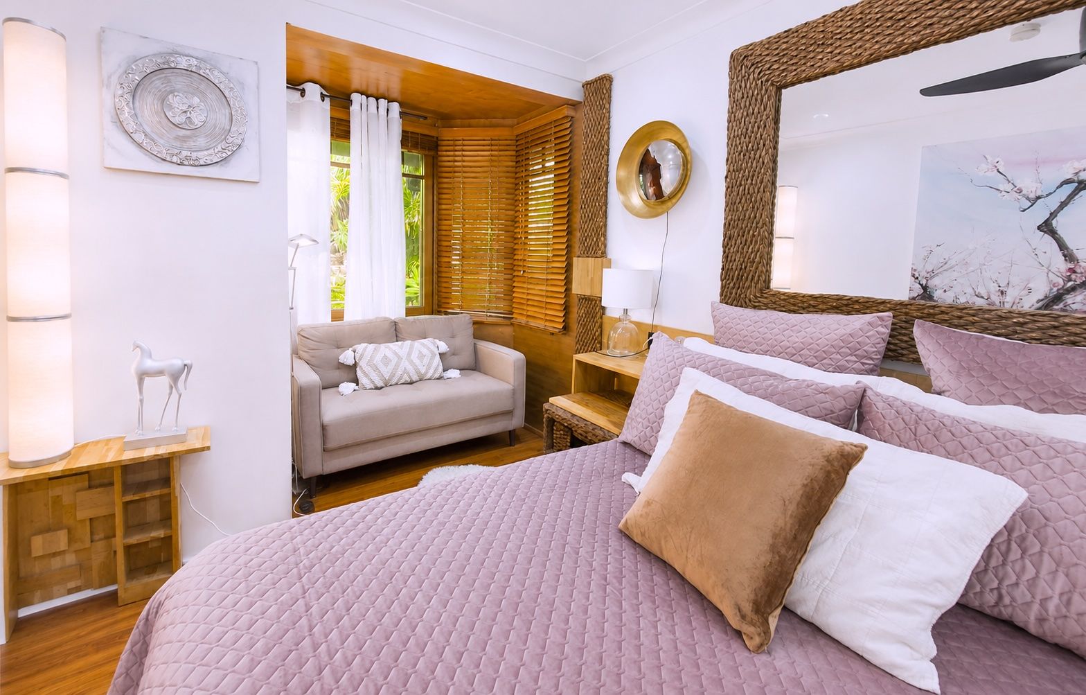 A bedroom with a large bed, a sofa, a bedside table, a lamp, and a mirror.
