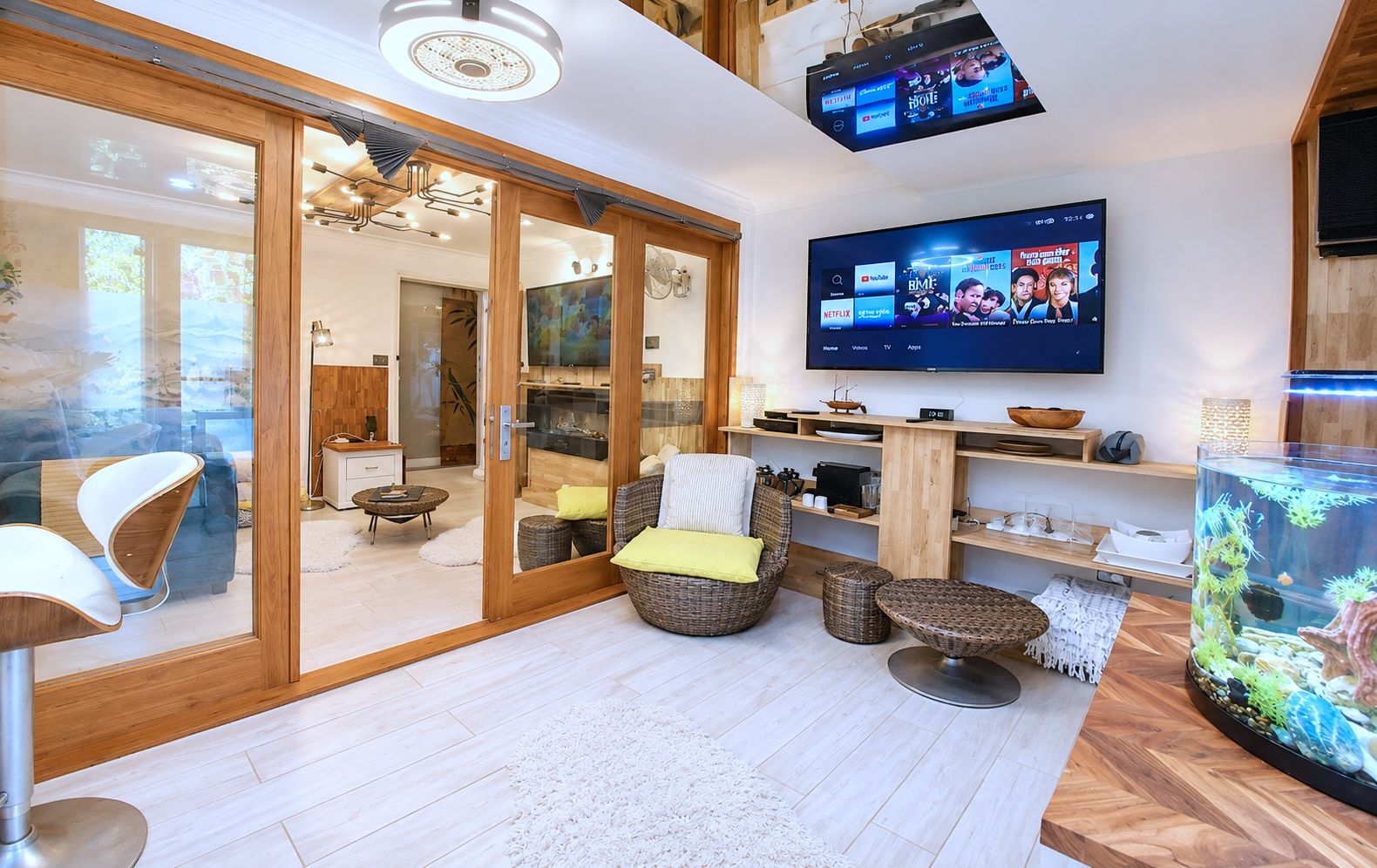 A modern living room with a flat-screen TV mounted on the wall, a large fish tank, and a sliding glass door leading to a dining area.