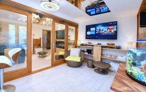 Een moderne woonkamer met een flatscreen televisie aan de muur, een groot aquarium en een schuifdeur die leidt naar een eethoek.