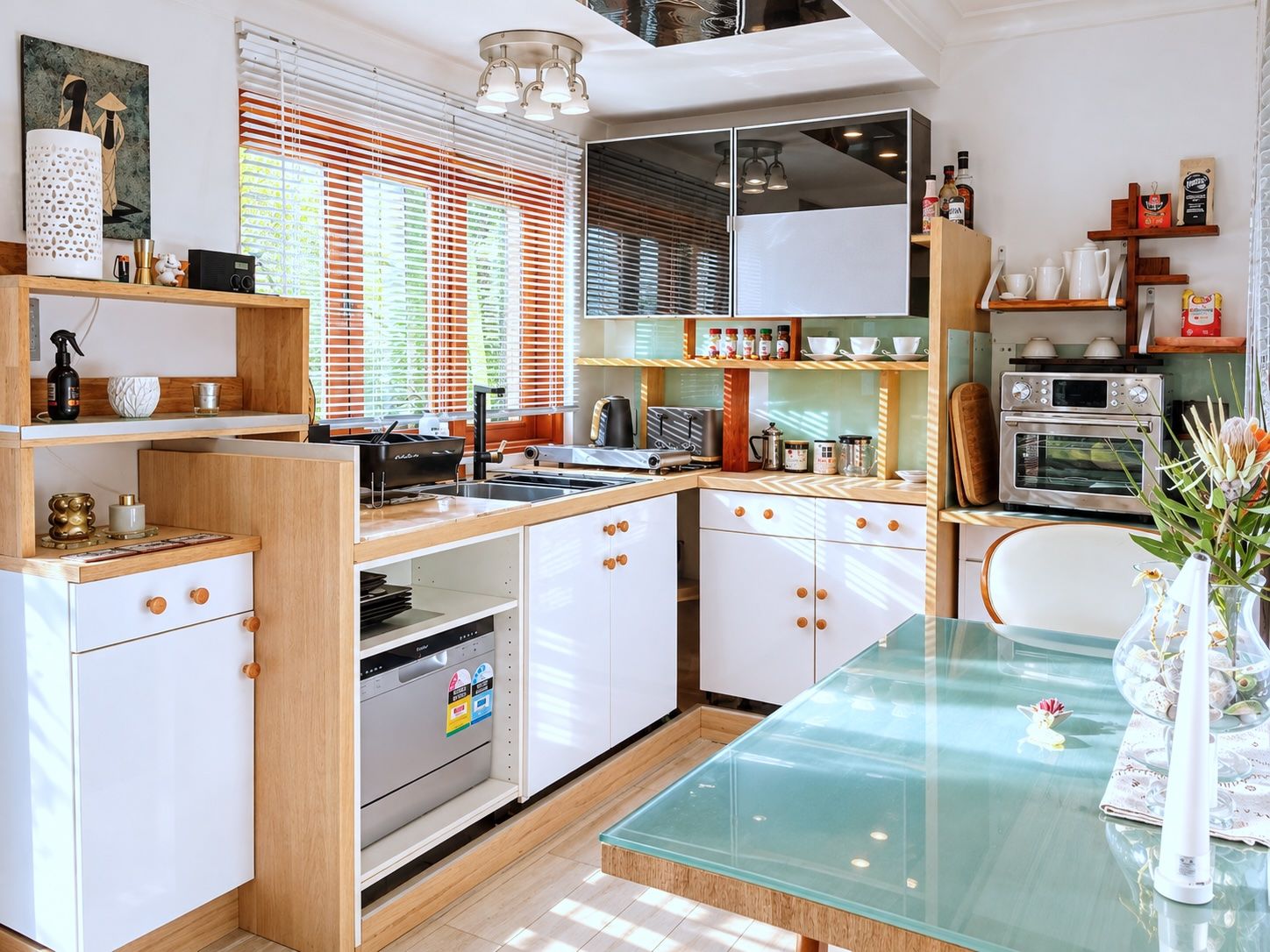 Ett modernt kök med ett matbord i glas, inbyggda vitvaror och ett stort utbud av köksredskap.