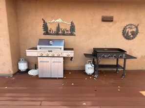 A barbecue setup with a grill and a portable table, two propane tanks, and a wall mural.