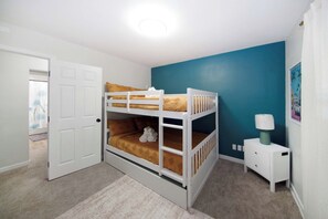 Uma cama beliche em um quarto com porta branca, parede de destaque verde-água e uma pequena mesa de cabeceira com luminária.