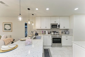 A modern kitchen with white cabinetry, stainless steel appliances, and pendant lighting. - Private Pool, Pickleball, Mini Golf, Game Room, Near AMI (Bradenton)