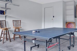 A ping pong table with a ball and paddle, two wooden chairs, and a white door in a room with white walls and a concrete floor. - 3BR 2 Bath Ranch-style house in Salida - Sleeps 7 (Salida)