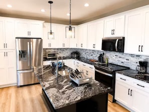 A modern kitchen with white cabinets, stainless steel appliances, a marble countertop, and pendant lighting. - Lake Cumberland Views by Lee’s Ford Marina 5BR, 3 Decks, Sleeps 10, Pet Friendly (Nancy)