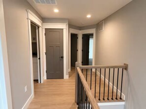 A hallway with a wooden floor, white walls, and a wooden railing. There are doors leading to other rooms. - Lake Cumberland Views by Lee’s Ford Marina 5BR, 3 Decks, Sleeps 10, Pet Friendly (Nancy)