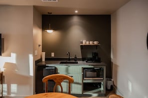 Eine kompakte Küche mit integriertem Mikrowellenherd, einer Kaffeemaschine und einem Regal mit Tassen.