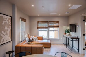A modern living room with a sofa, a dining table, and a TV mounted on the wall.