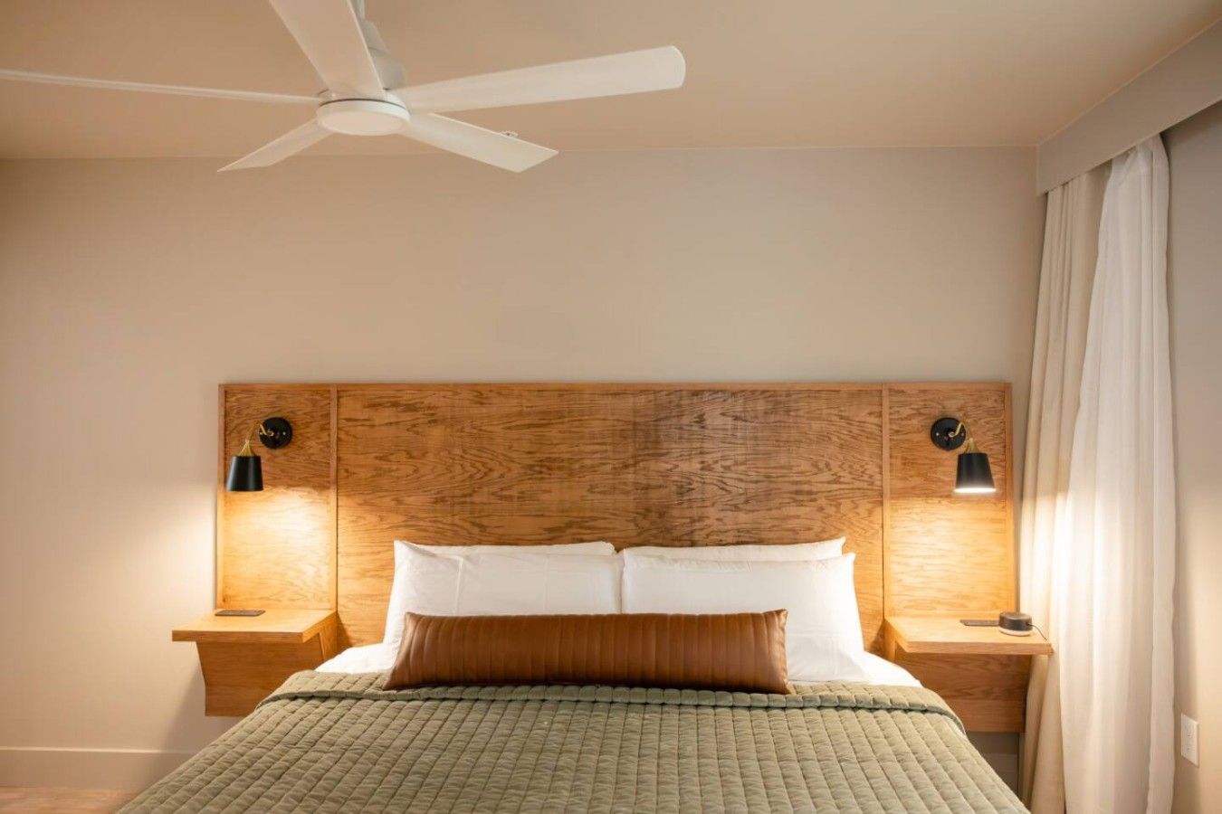 A bedroom with a wooden headboard, two bedside lamps, a bed with pillows, and a ceiling fan.