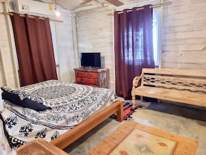 A room with a bed, a wooden bench, a television on a stand, and a window with curtains. - Incredible Loft on the Beach! (Bocas del Toro)