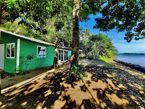 A green wooden cabin with a window and a door, surrounded by trees and a beach. - Incredible Loft on the Beach! (Bocas del Toro)