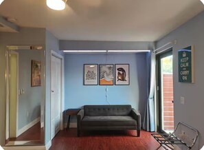 Ein Zimmer mit einem dunklen Sofa, einem kleinen Tisch und einer Wand mit drei gerahmten Kunstwerken.