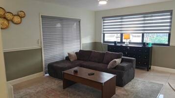 A living room with a sofa, coffee table, and a window with blinds.