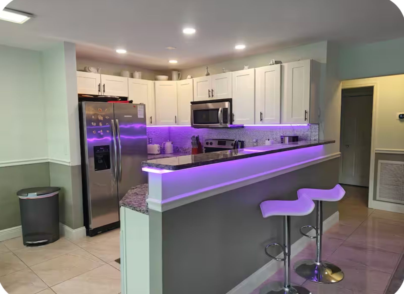 Une cuisine moderne dotée d’un îlot central, d’appareils électroménagers intégrés et d’un éclairage violet sous les meubles hauts.