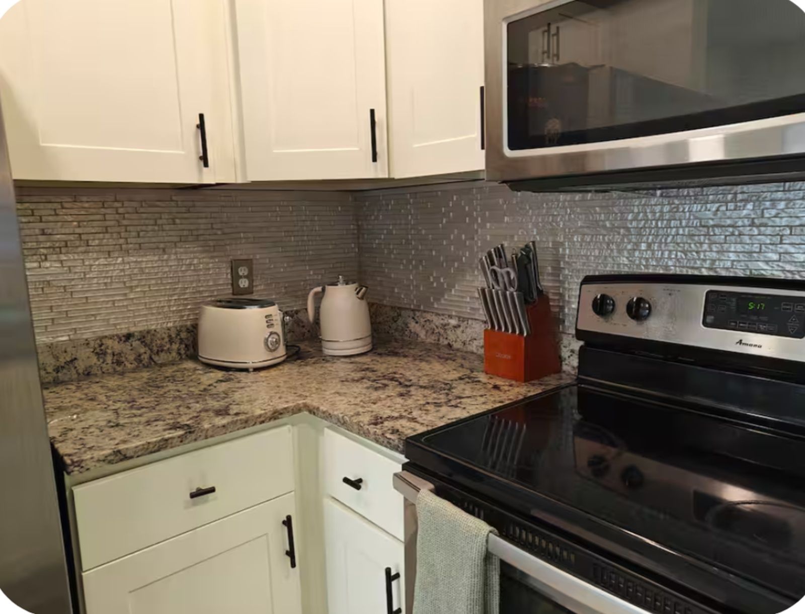 A kitchen with white cabinets, a granite countertop, a toaster, a kettle, and a stove.