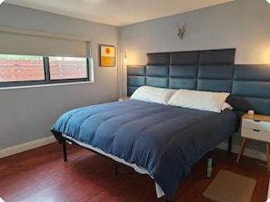 Ein Schlafzimmer mit einem Bett, einem Nachttisch, einer Wanduhr und einem Fenster mit Jalousien.