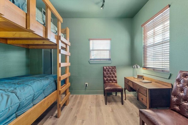 Een kamer met stapelbedden, een bureau, een stoel en een raam met jaloezieën.