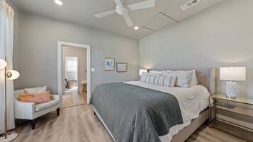 Ein Schlafzimmer mit einem Bett, Nachttischen, einem Sessel, einem Deckenventilator und einer Tür zu einem anderen Raum.