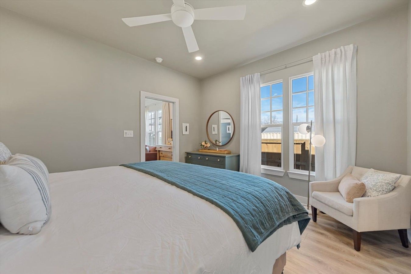 A bedroom with a bed, a chair, a dresser, a ceiling fan, and a window with curtains.