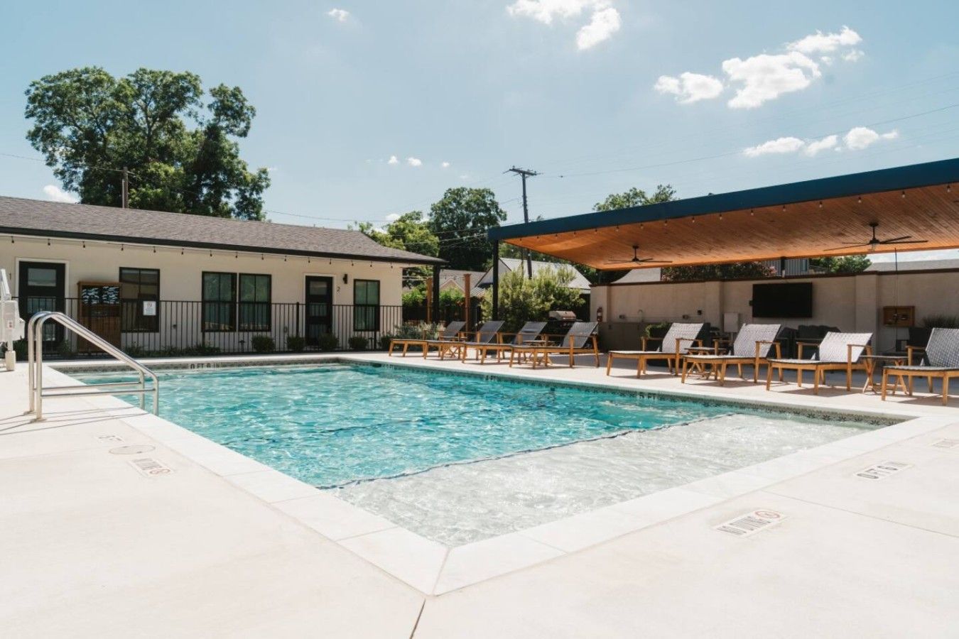 A swimming pool with lounge chairs and a covered area, surrounded by buildings.