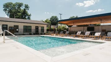 A swimming pool with lounge chairs and a covered area, surrounded by buildings.