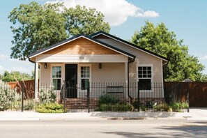 Een gelijkvloers huis met een puntige kap, een veranda en een omheinde tuin.