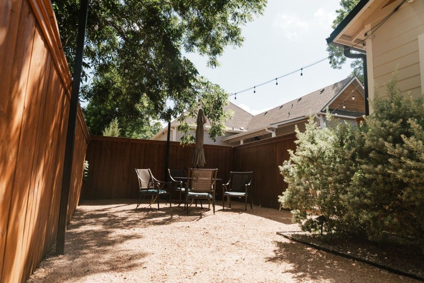 Een achtertuin met een houten schutting, een patio tafel met stoelen en een kleine altijdgroene boom.