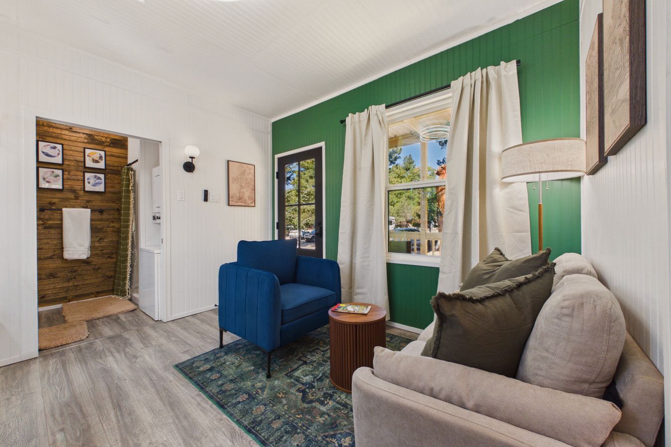 A room with a blue chair, a beige sofa, a wooden door, and a window with curtains.