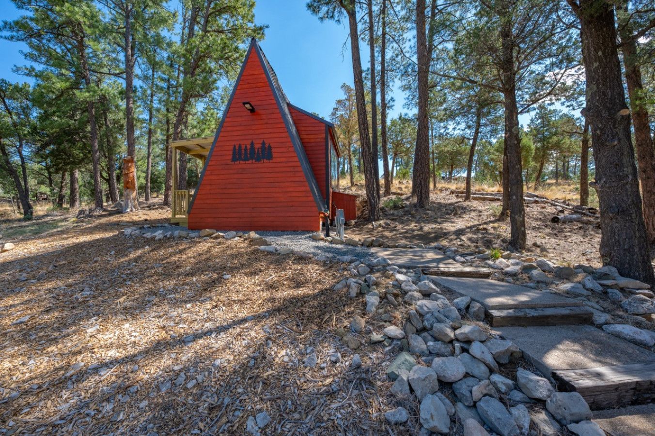 Une cabane rouge avec un toit triangulaire, entourée d’arbres.
