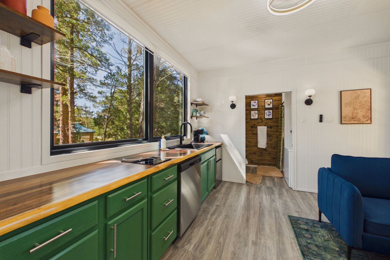 Une cuisine moderne avec des meubles de couleur verte, un plan de travail en bois et une grande fenêtre donnant sur les arbres.