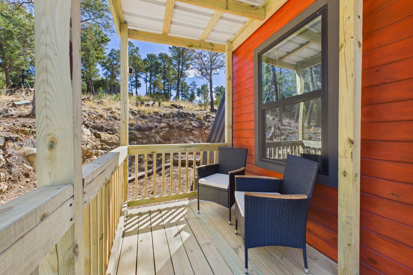 Een houten terras met twee rieten stoelen en een tafel, met uitzicht op een natuurlandschap.