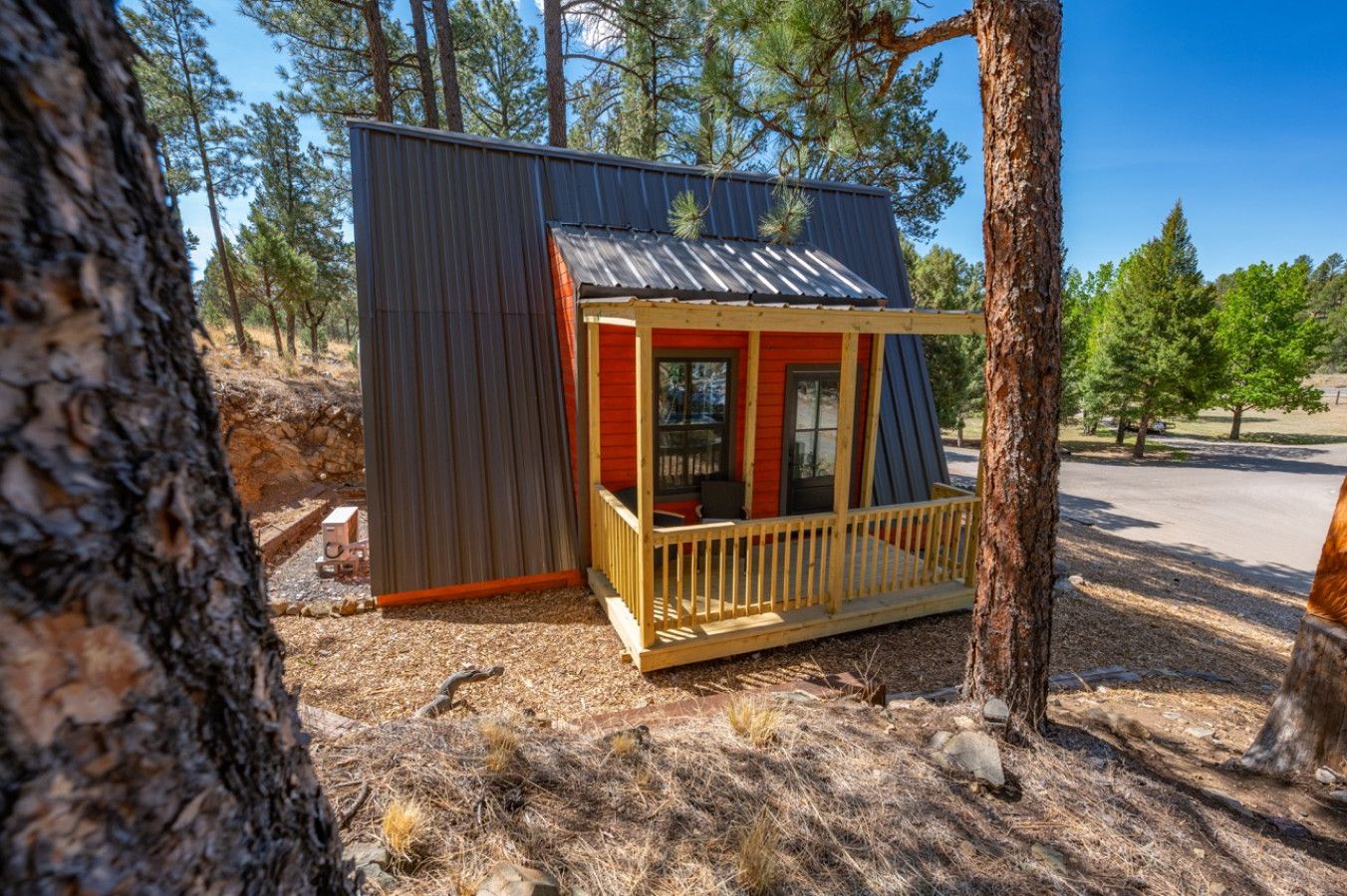 A small cabin with a wooden deck and a metal roof, surrounded by trees.