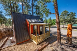 A small cabin with a porch, surrounded by trees.