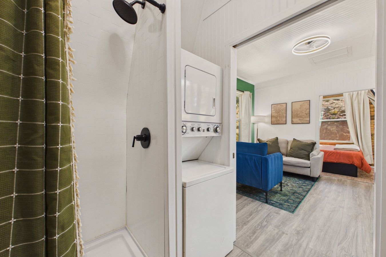A hotel room with a shower, a washing machine, a bed, and a sofa.