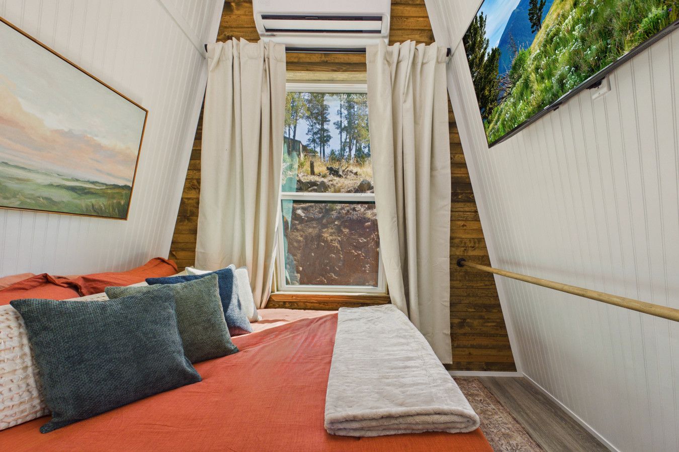 A bedroom with a bed, pillows, a window, and a painting.