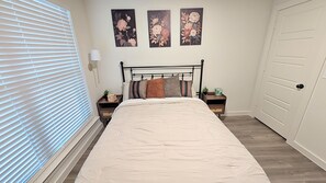 A bedroom with a bed, a nightstand, a bedside table, a lamp, and three wall-mounted floral paintings. - Auburn House - New 4BR Near Texas Tech (Lubbock)