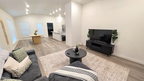 A modern living room with a flat-screen TV, dark sofas, and a coffee table. - Auburn House - New 4BR Near Texas Tech (Lubbock)