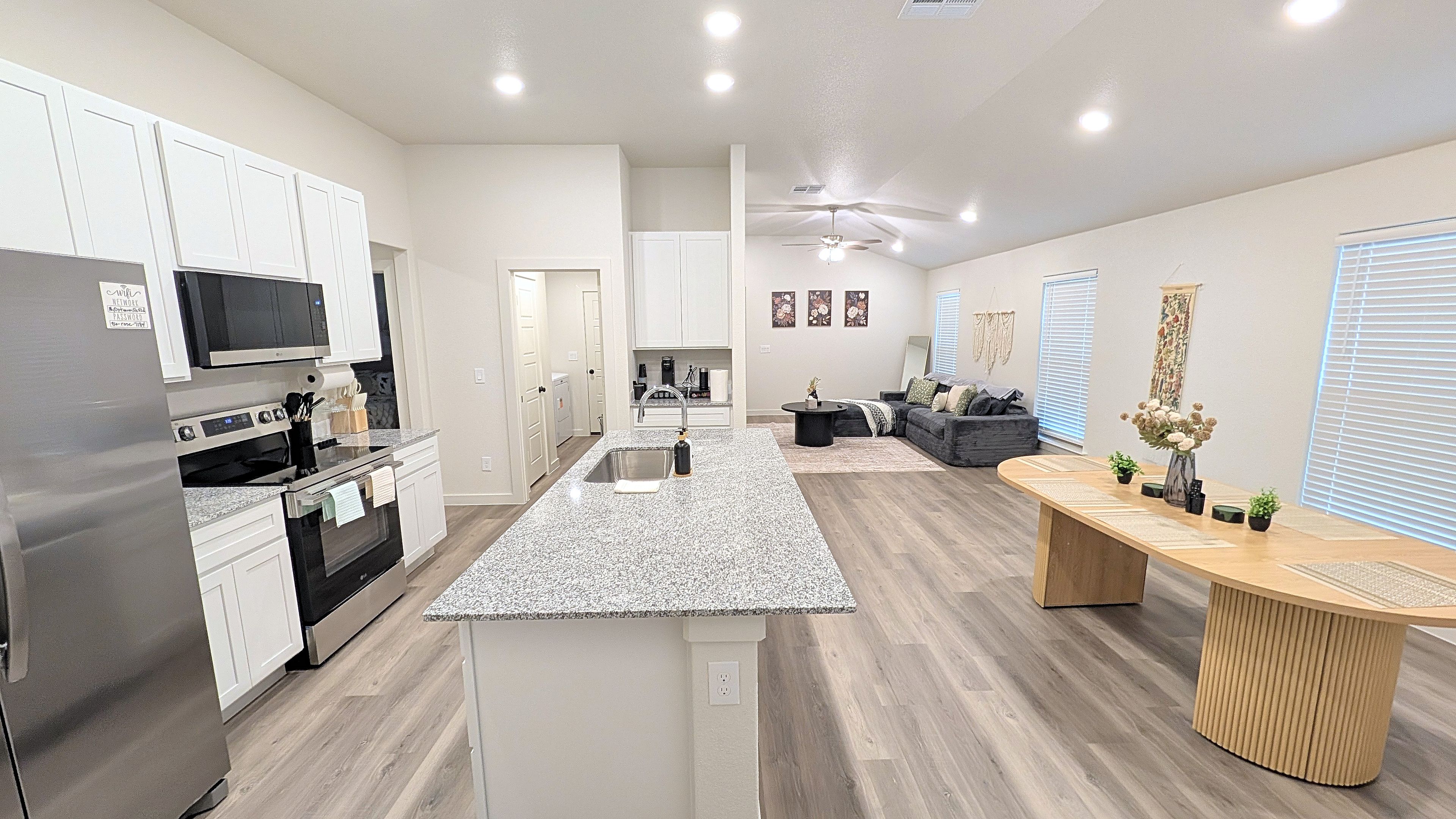 A modern kitchen with a central island, a dining area with a wooden table, and a living room with a sofa.
