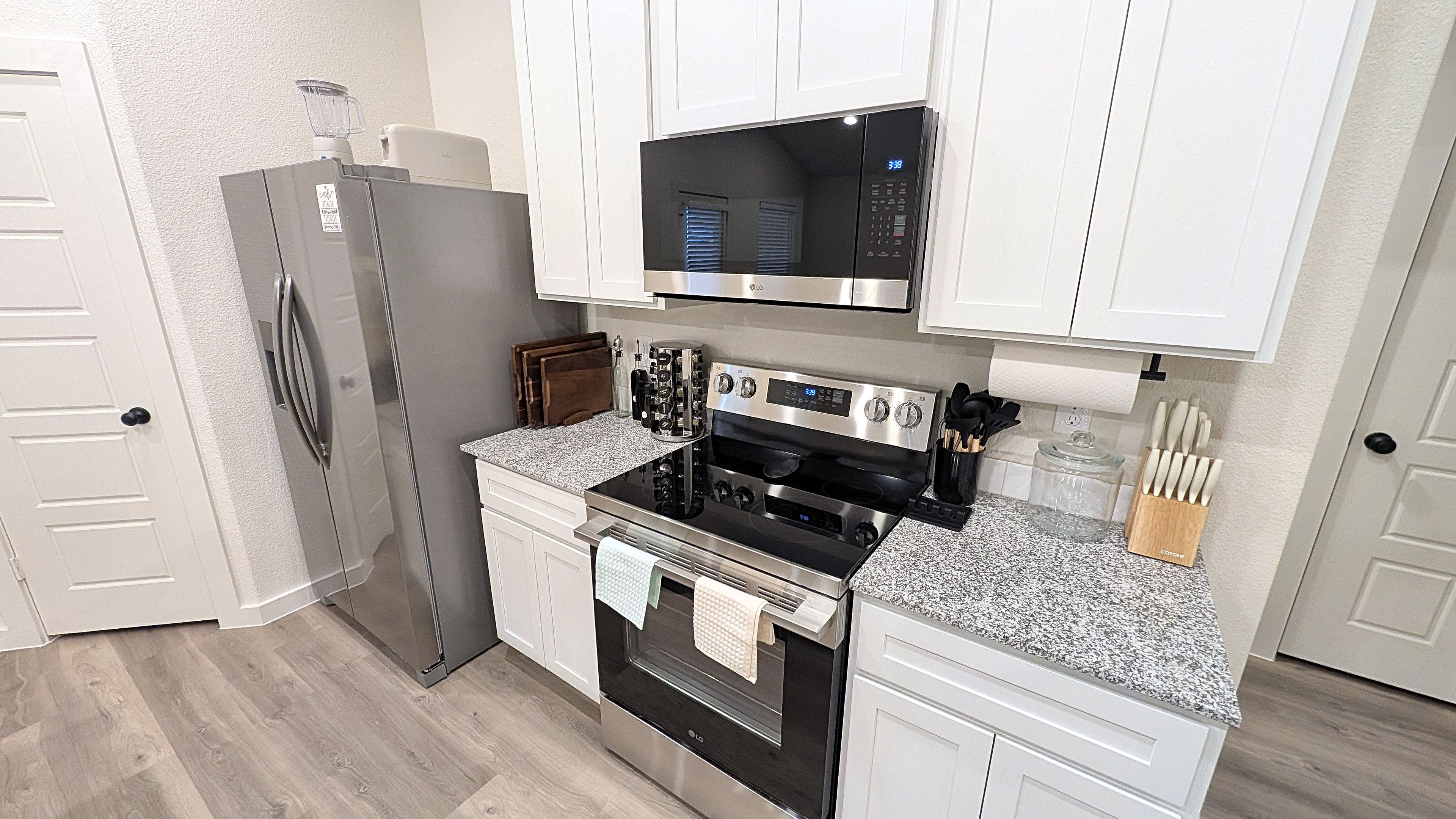 A modern kitchen with white cabinets, a stainless steel refrigerator, an oven, a microwave, and a granite countertop.