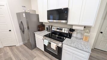 A modern kitchen with white cabinets, a stainless steel refrigerator, an oven, a microwave, and a granite countertop.
