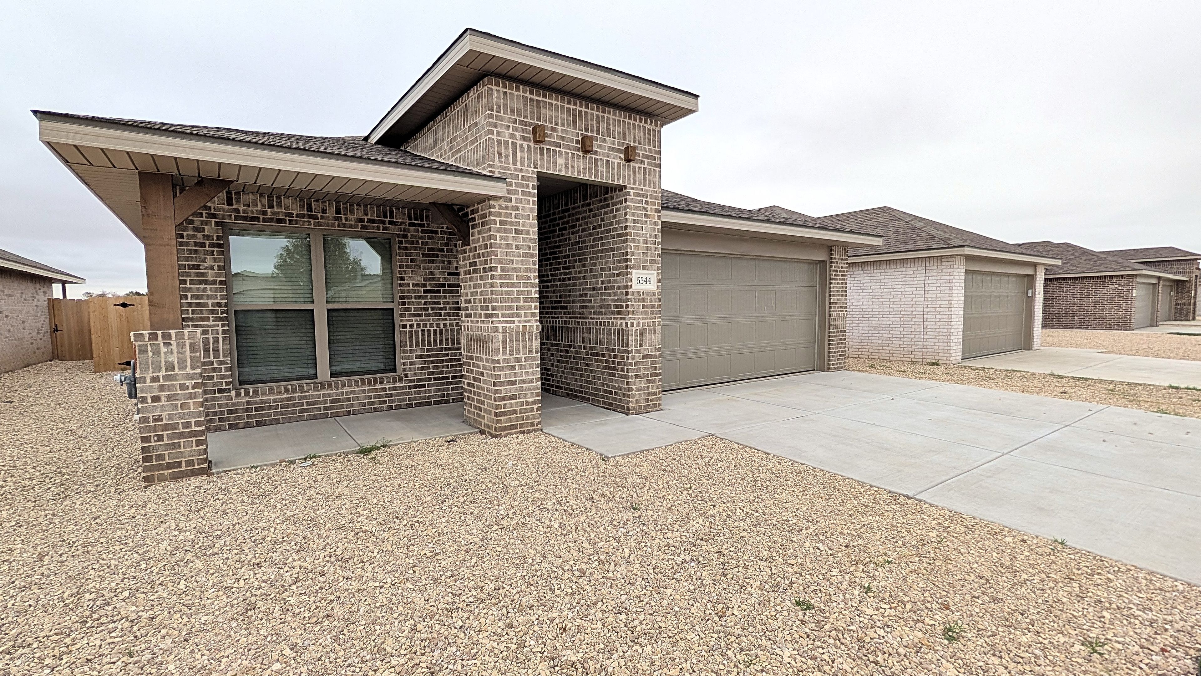 A residential building with a brick facade, a garage, and a gravel driveway.