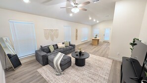 A spacious living room with a grey sectional sofa, a round coffee table, and a ceiling fan. - Auburn House - New 4BR Near Texas Tech (Lubbock)